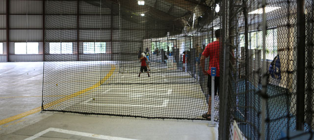 Side view of several batters hitting balls in cages