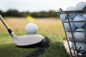Bucket of balls next to golf ball teed up on hitting mat at driving range 