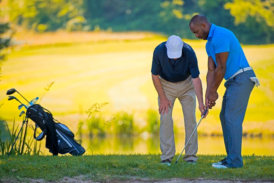 Golf teacher helping other golfer with swing